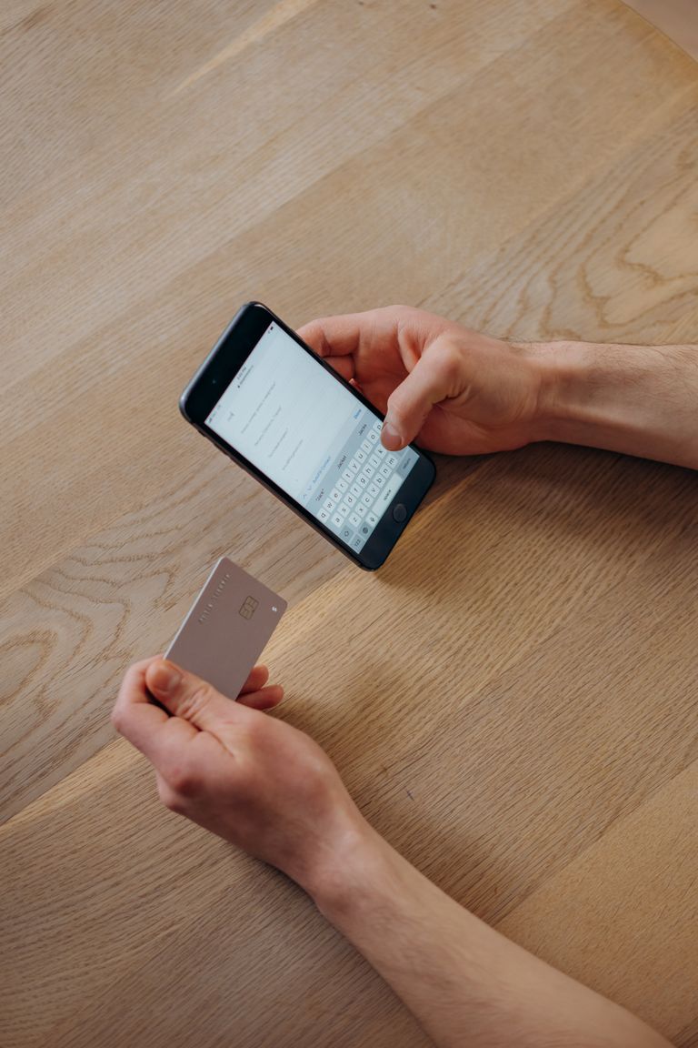 A person holds a smartphone and credit card for online shopping on a wooden table.