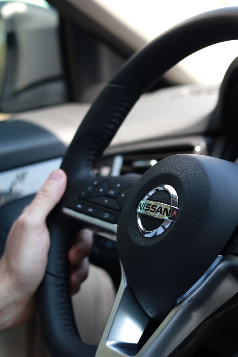 Focused shot of a hand gripping a Nissan steering wheel, inside a car.
