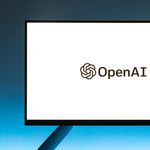 Minimalistic display of OpenAI logo on a monitor with a gradient blue background, representing modern technology.