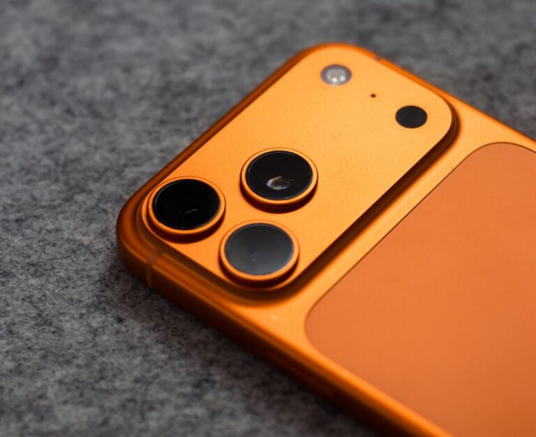 Stylish orange smartphone with triple camera lens on a gray fabric background, perfect for tech themes.