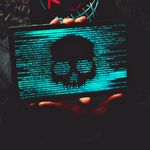 A mysterious person in a neon mask holds a tablet displaying a digital skull.
