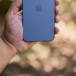 Close-up of a hand holding a smartphone with a blurred nature background, emphasizing technology in outdoor settings.