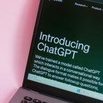 Close-up of a laptop with ChatGPT introduction on screen against a pink background.