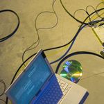 Top view of a laptop with cables and a CD on a concrete floor, highlighting technology and data concepts.