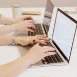 Two people typing on laptops in an office setting, emphasizing teamwork and productivity.
